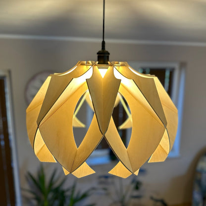 Close-up of a large wooden pendant lamp with a modern, flower-like design. The natural birch wood creates soft, warm light patterns on the ceiling, enhancing the room&#39;s ambiance.